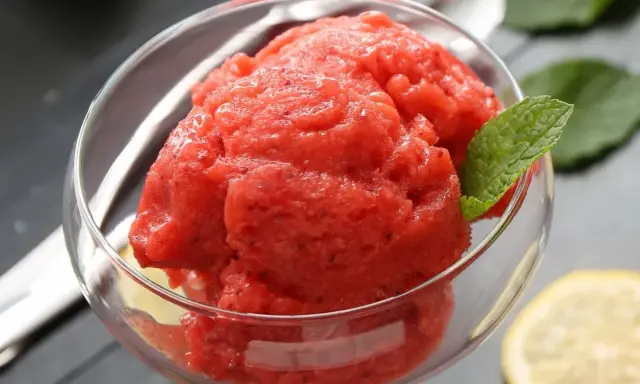 Orzeźwiający sorbet z arbuza w szklanej miseczce, ozdobiony listkiem mięty i plasterkiem cytryny. Idealny na upalne dni.