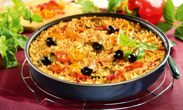 Pyszna paella z kurczakiem, ryżem, papryką, oliwkami i ziołami, podana w głębokiej patelni.