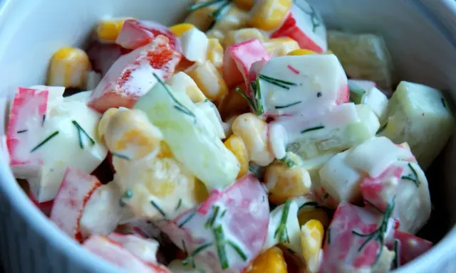 Pyszna sałatka z surimi, kukurydzy, ogórka i papryki, polana kremowym sosem i posypana koperkiem.