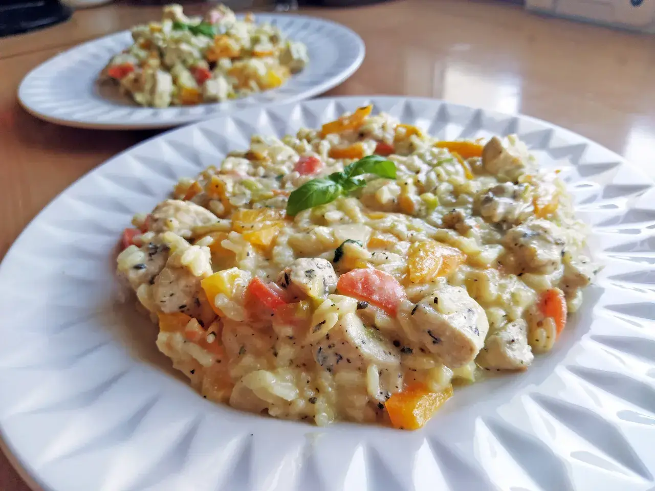 Pyszne, klasyczne risotto z kurczakiem i kolorowymi warzywami, udekorowane listkiem bazylii. Idealne na obiad.