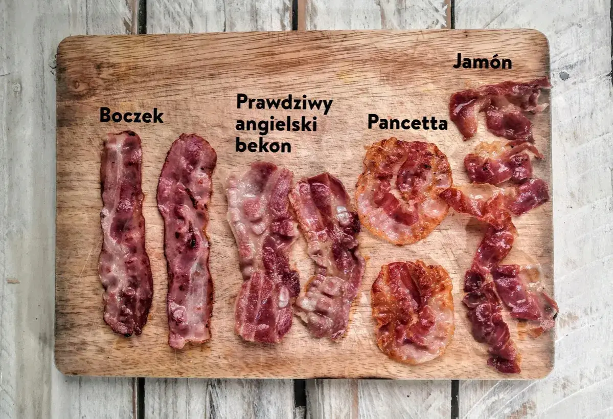 Na desce leżą różne rodzaje bekonu: boczek, prawdziwy angielski bekon, pancetta i jamón.