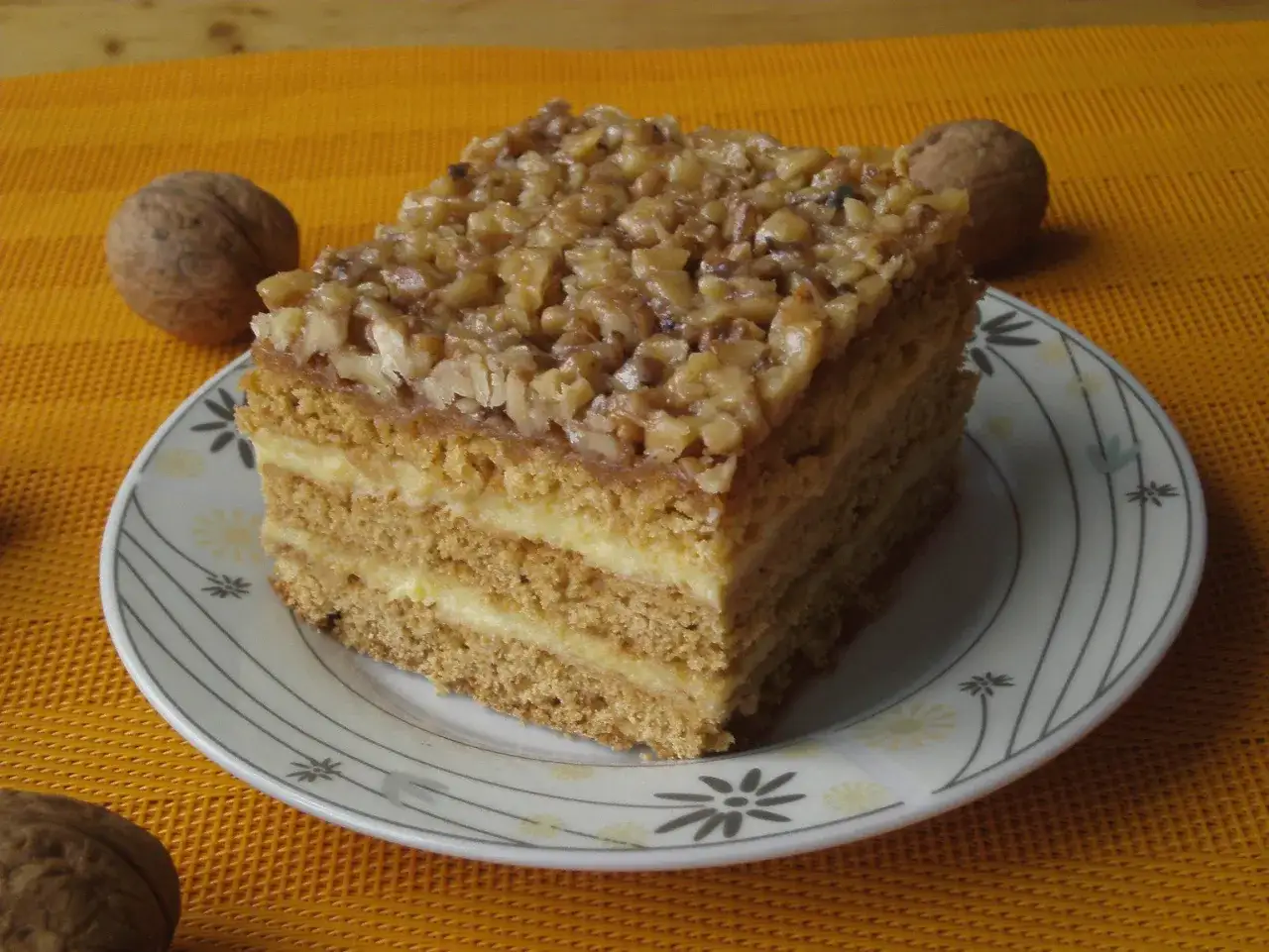 Pyszny kawałek miodownika z orzechami, jeden z 10 najlepszych ciast, na talerzyku z orzechami w tle.