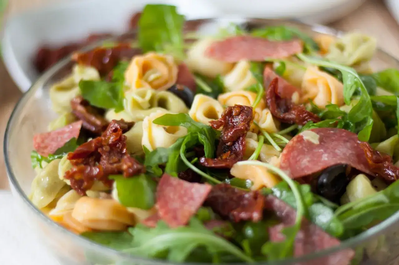 Pyszna sałatka z tortellini, rukolą, suszonymi pomidorami i salami. Idealna na letni obiad.