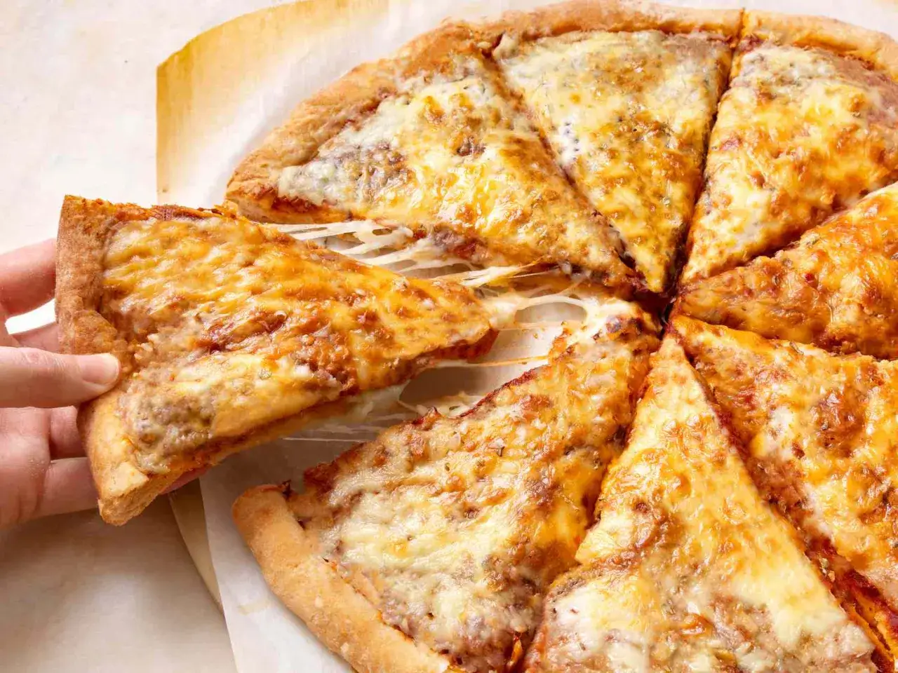 Domowa pizza przepis: ręka podnosi kawałek pysznej pizzy z ciągnącym się serem. Idealna na rodzinny obiad.