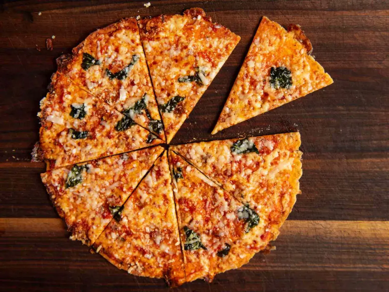 Chrupiąca pizza z tortilli, pokrojona na kawałki, z roztopionym serem i zielonymi liśćmi na drewnianej desce.
