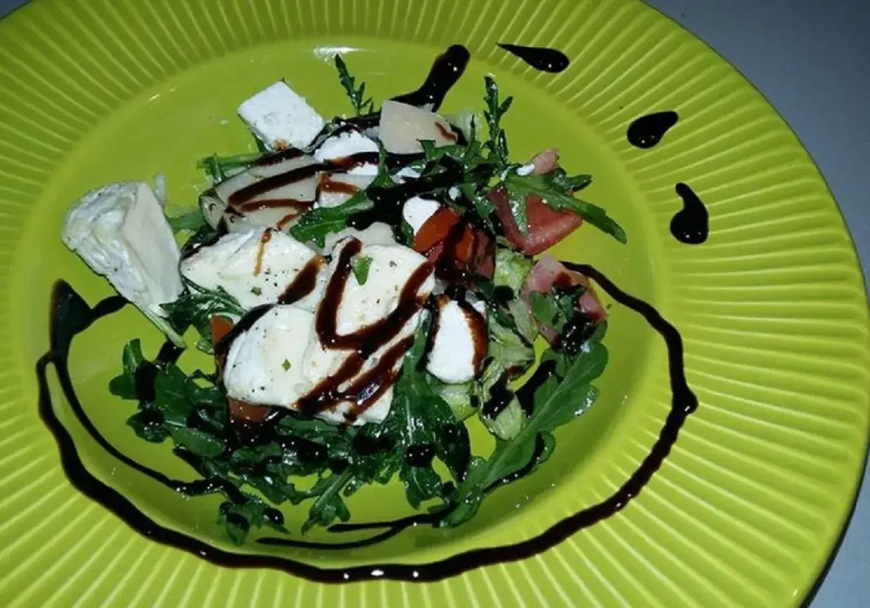 Pyszna sałatka z rukolą, mozzarellą i pomidorkami, polana sosem balsamicznym. Idealna na lekki posiłek.