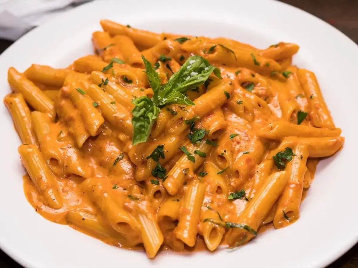 Penne alla vodka w kremowym sosie pomidorowym, udekorowane świeżą bazylią i natką pietruszki.