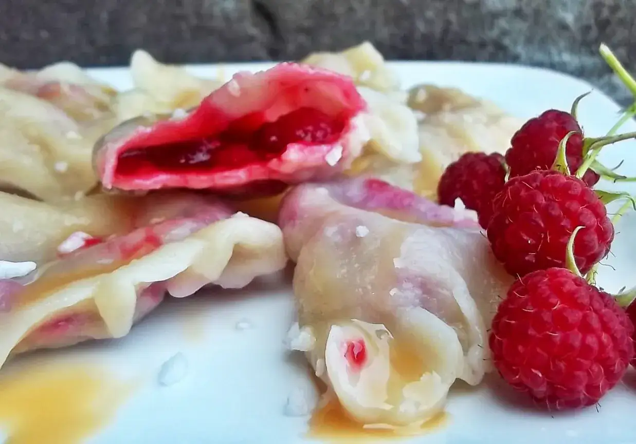 Pyszne pierogi z malinami, polane syropem, z dodatkiem świeżych malin. Letnia uczta na talerzu.