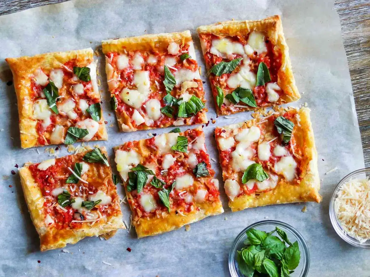 Sześć kwadratowych kawałk&oacute;w pysznej pizzy z ciasta francuskiego, z sosem pomidorowym, mozzarellą i bazylią.