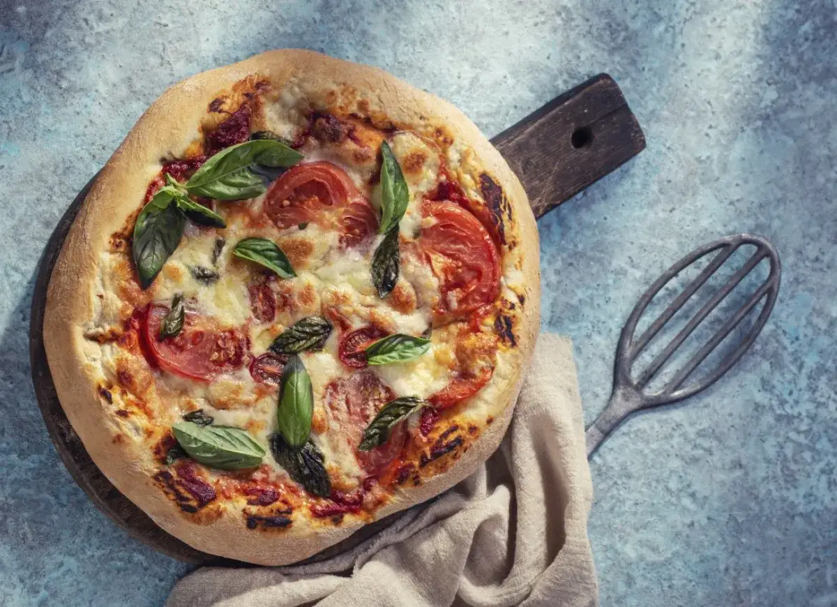 Pyszna pizza bez drożdży z pomidorami i bazylią, podana na drewnianej desce.