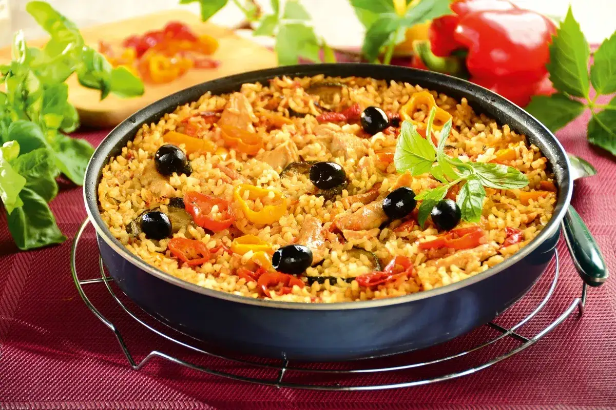 Pyszna paella z kurczakiem, ryżem, papryką, oliwkami i ziołami, podana w głębokiej patelni.