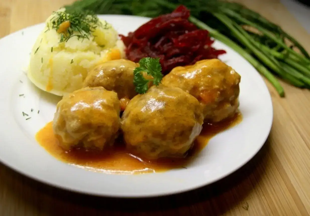 Pyszne klopsiki w sosie pomidorowym, podane z purée ziemniaczanym i buraczkami. Danie ozdobione natką pietruszki i koperkiem.