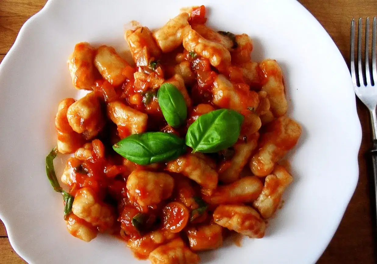 Pyszne gnocchi w sosie pomidorowym, udekorowane listkami bazylii. Idealne danie na szybki obiad.