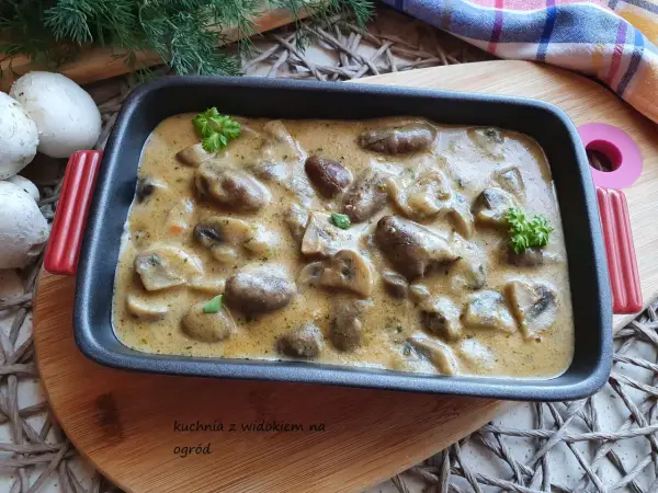 Gulasz z serc drobiowych w kremowym sosie, udekorowany natką pietruszki. Obok leżą świeże pieczarki i gałązki koperku.
