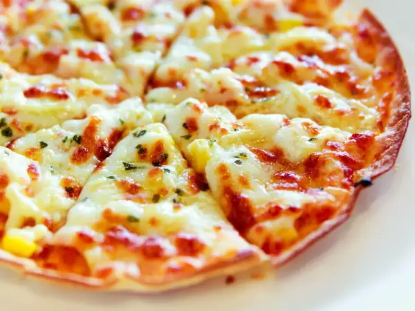 Pyszna pizza z tortilli, obficie posypana serem i ziołami, pokrojona na trójkątne kawałki.