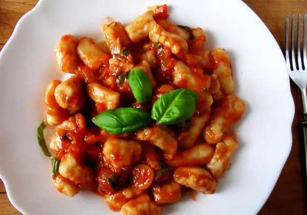 Pyszne gnocchi w sosie pomidorowym, udekorowane świeżą bazylią. Idealne danie na szybki obiad.
