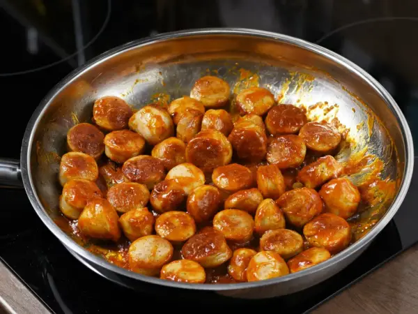 Kiełbasa z cebulą duszona na patelni w sosie. Aromatyczne kawałki mięsa w bogatym, pomarańczowym sosie.